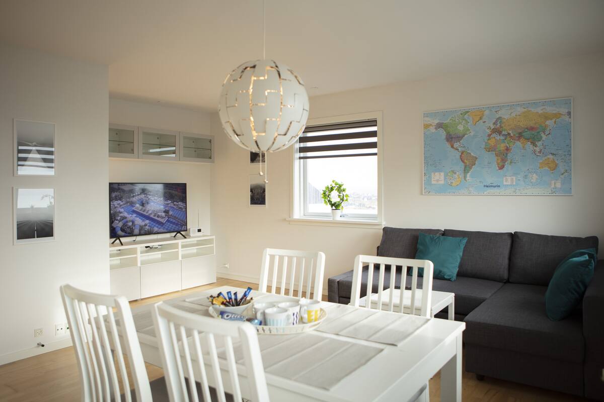 En moderne stue med spiseplads, et fladskærms-tv, et verdenskort og en dekorativ globuslampe.