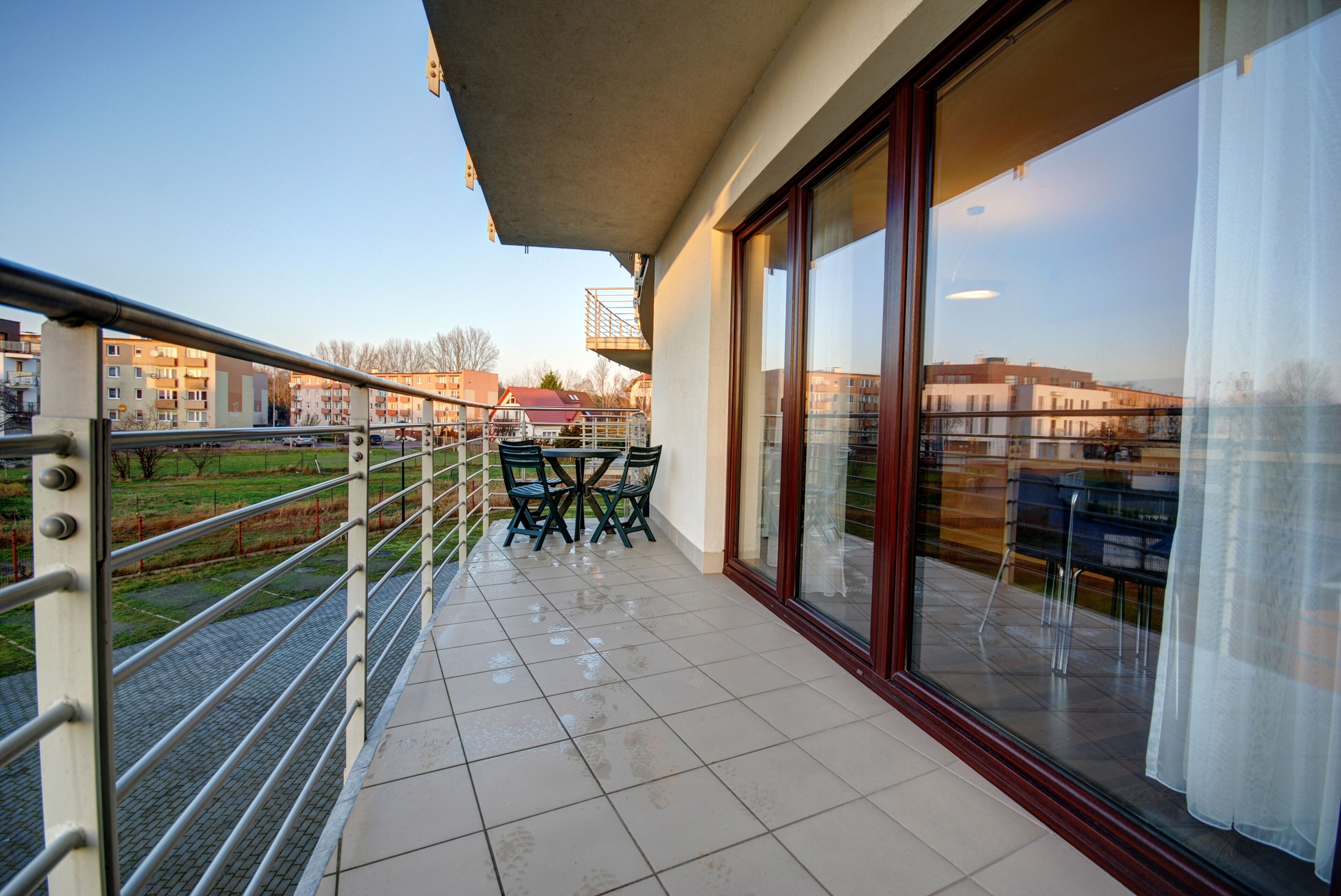 A balcony with a view of a residential area, a table with chairs, and a railing.