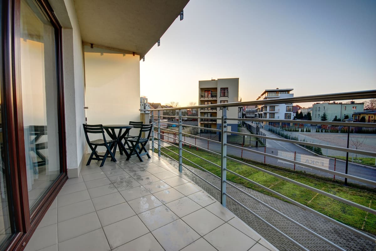A balcony with a table and chairs, offering a view of a cityscape and a road.
