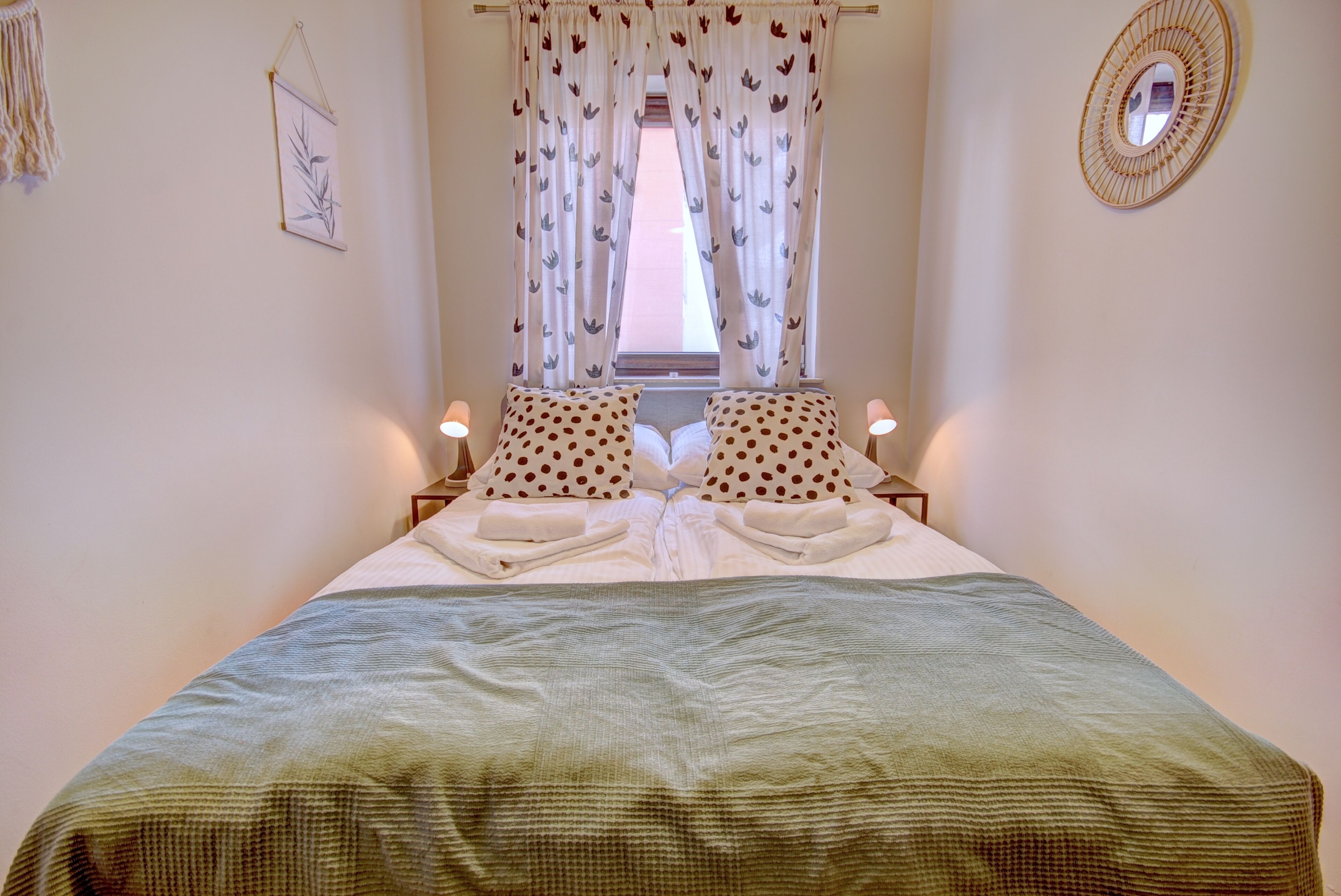 A neatly made bed with a polka dot pillow set, a green blanket, and a window with floral curtains.