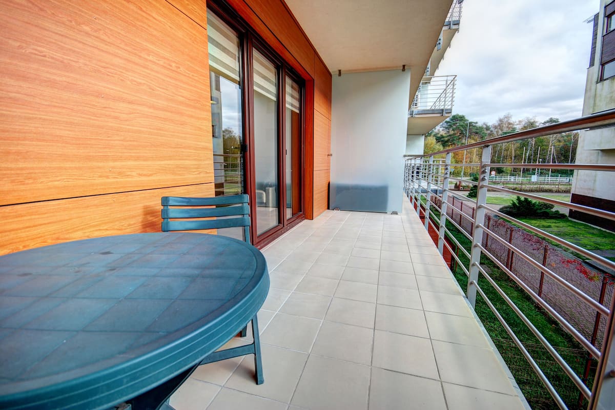 A balcony with a table and chairs, a sliding glass door, and a view of a park.