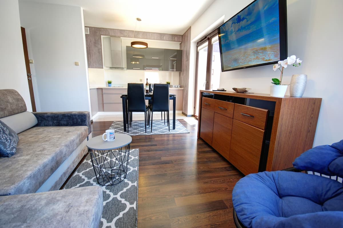A modern living room with a sofa, a blue armchair, a coffee table, and a dining area with chairs and a table.