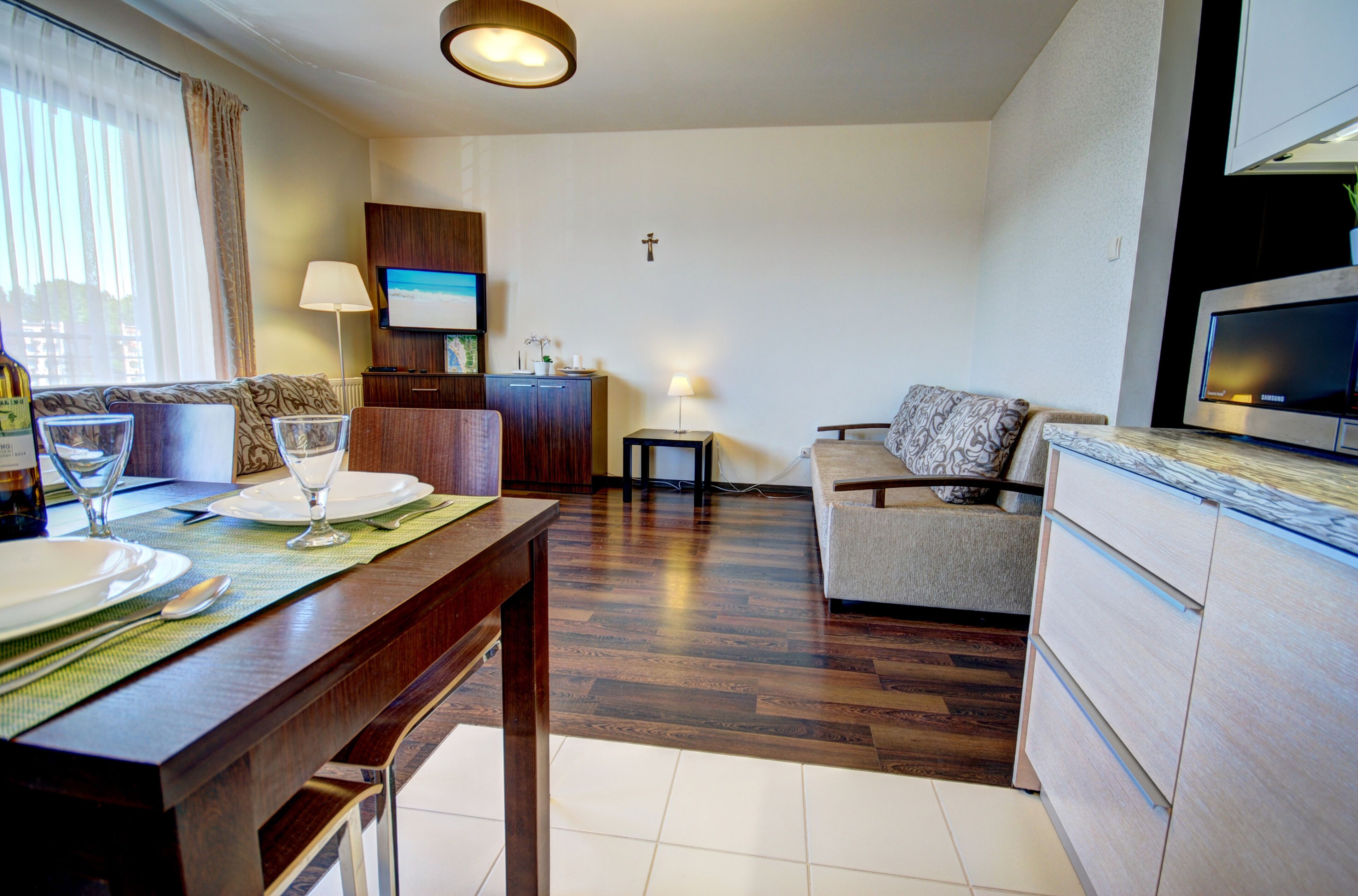 Habitación de hotel con zona de comedor, sofá, televisor y una cruz en la pared.