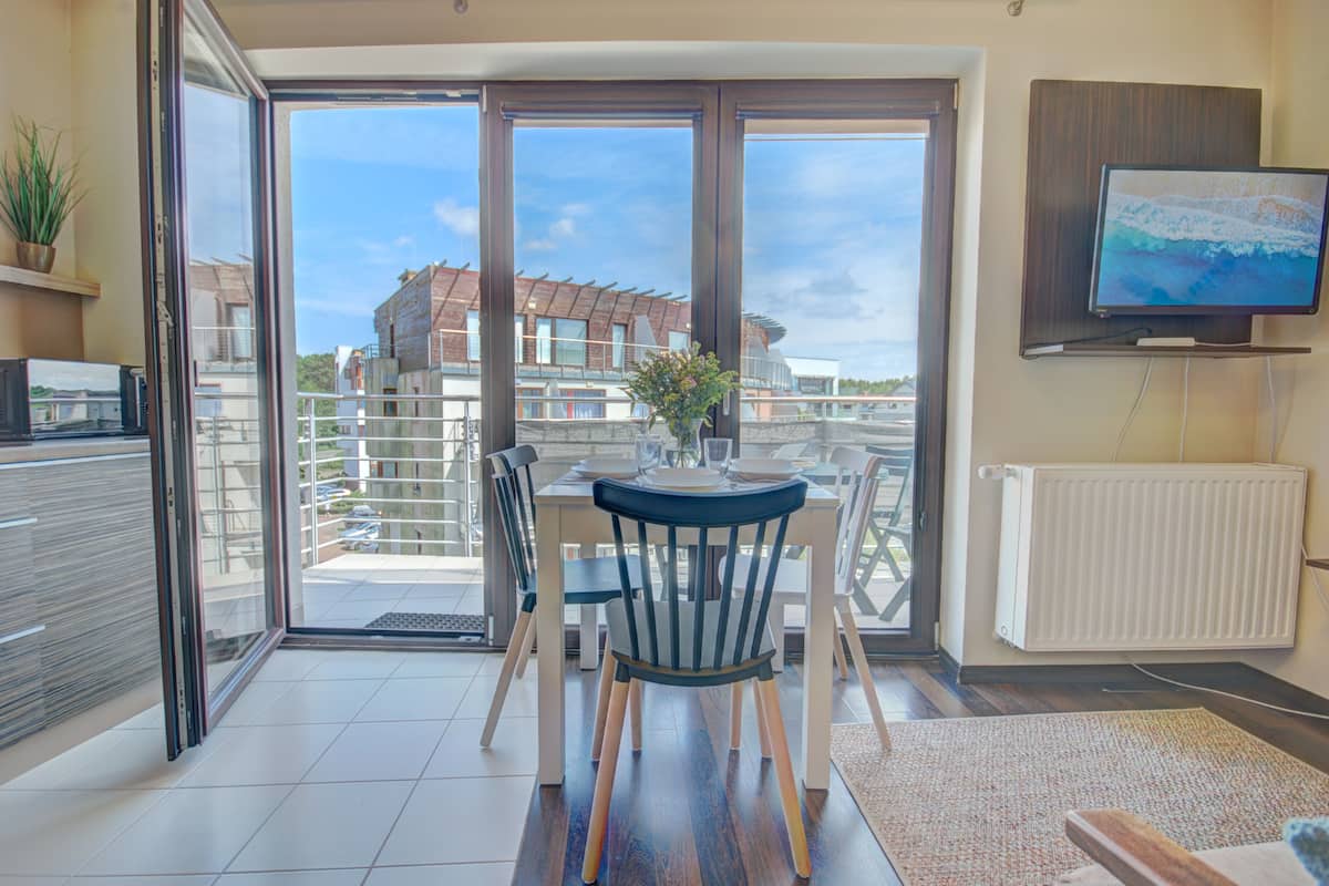 A modern dining area with a table and chairs, a potted plant, and a view of buildings through large windows.