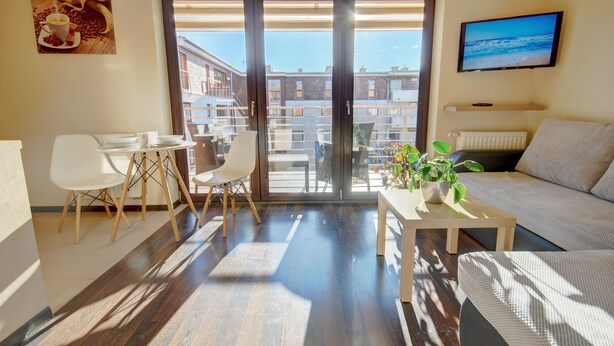 A modern living room with a sofa, a coffee table with a plant, and a dining area with chairs and a table. - HelApart - Apartamenty Foka (Hel)
