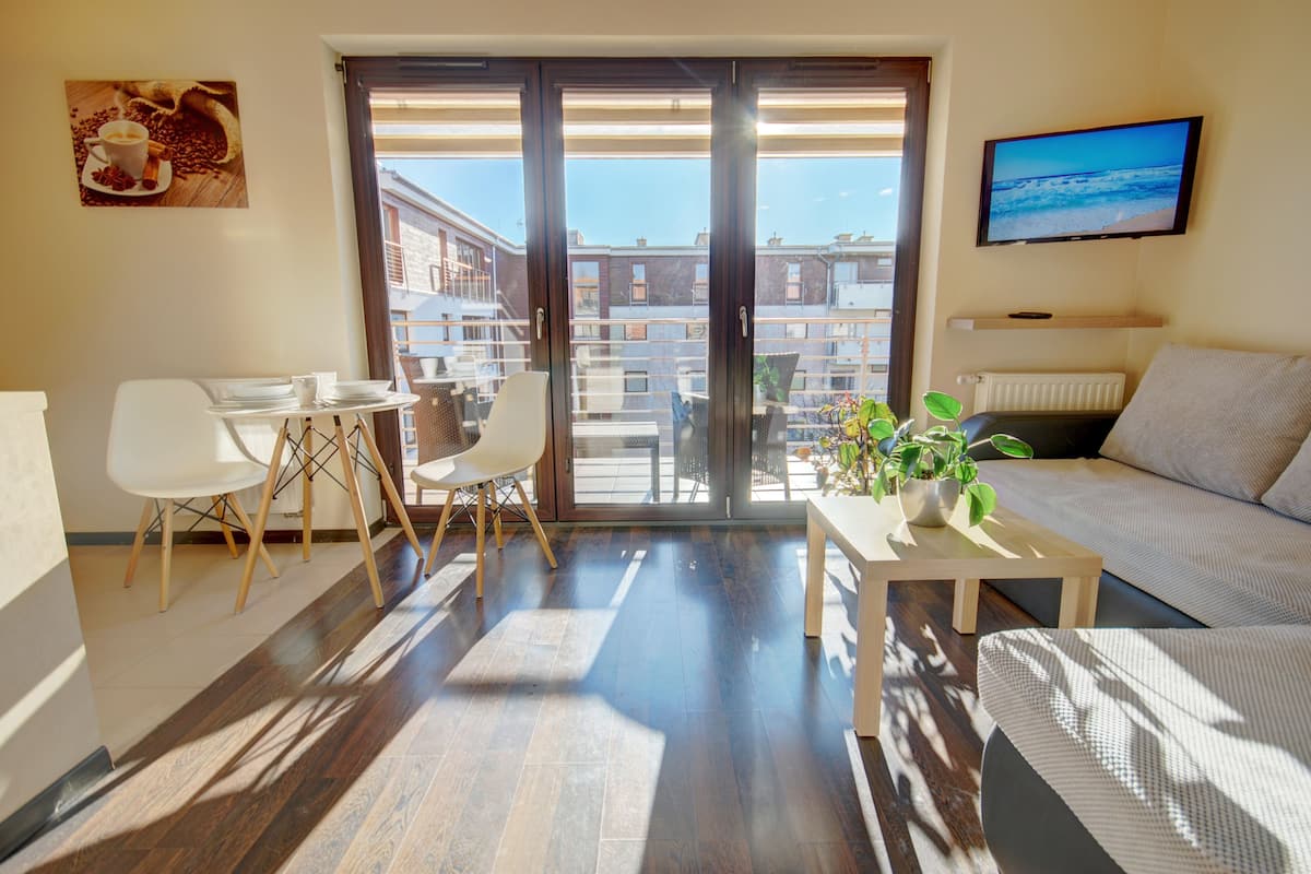 A modern living room with a sofa, a coffee table with a plant, and a dining area with chairs and a table.