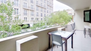 Ein Balkon mit Tisch und Stühlen, mit Blick auf ein Gebäude und Grünflächen.