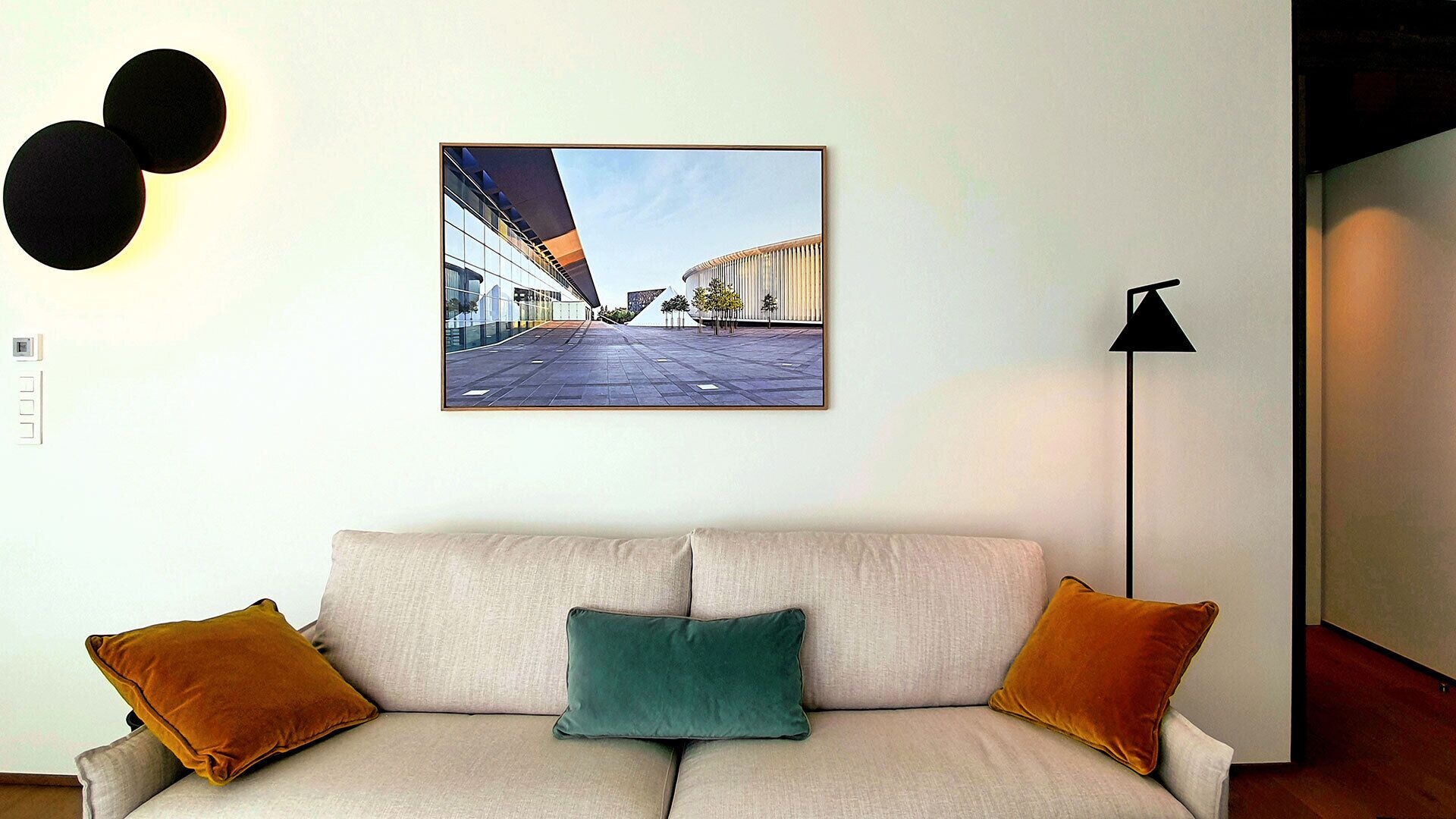 A living room with a sofa, two cushions, a framed photograph on the wall, and a floor lamp.