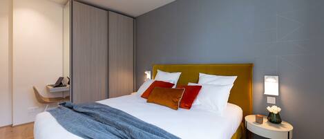 A modern hotel room with a large bed, a bedside table with a lamp, and a chair.