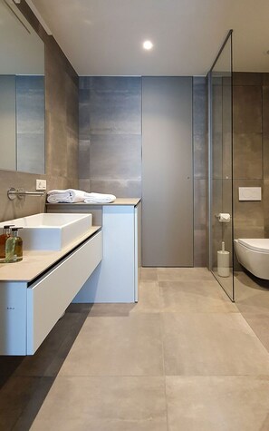 A modern bathroom with a large mirror, a white sink, and a glass-enclosed shower.