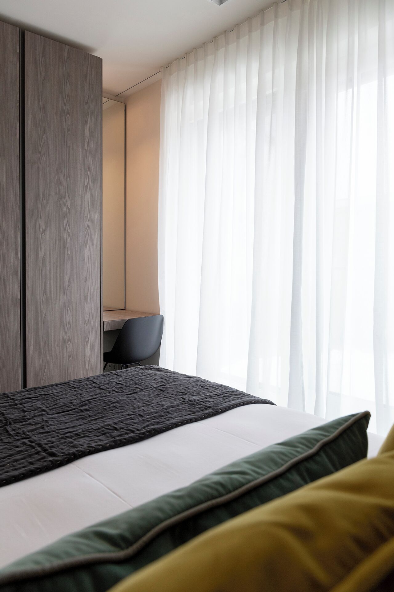 Une chambre moderne avec un grand lit, une armoire en bois, un bureau et des rideaux légers.