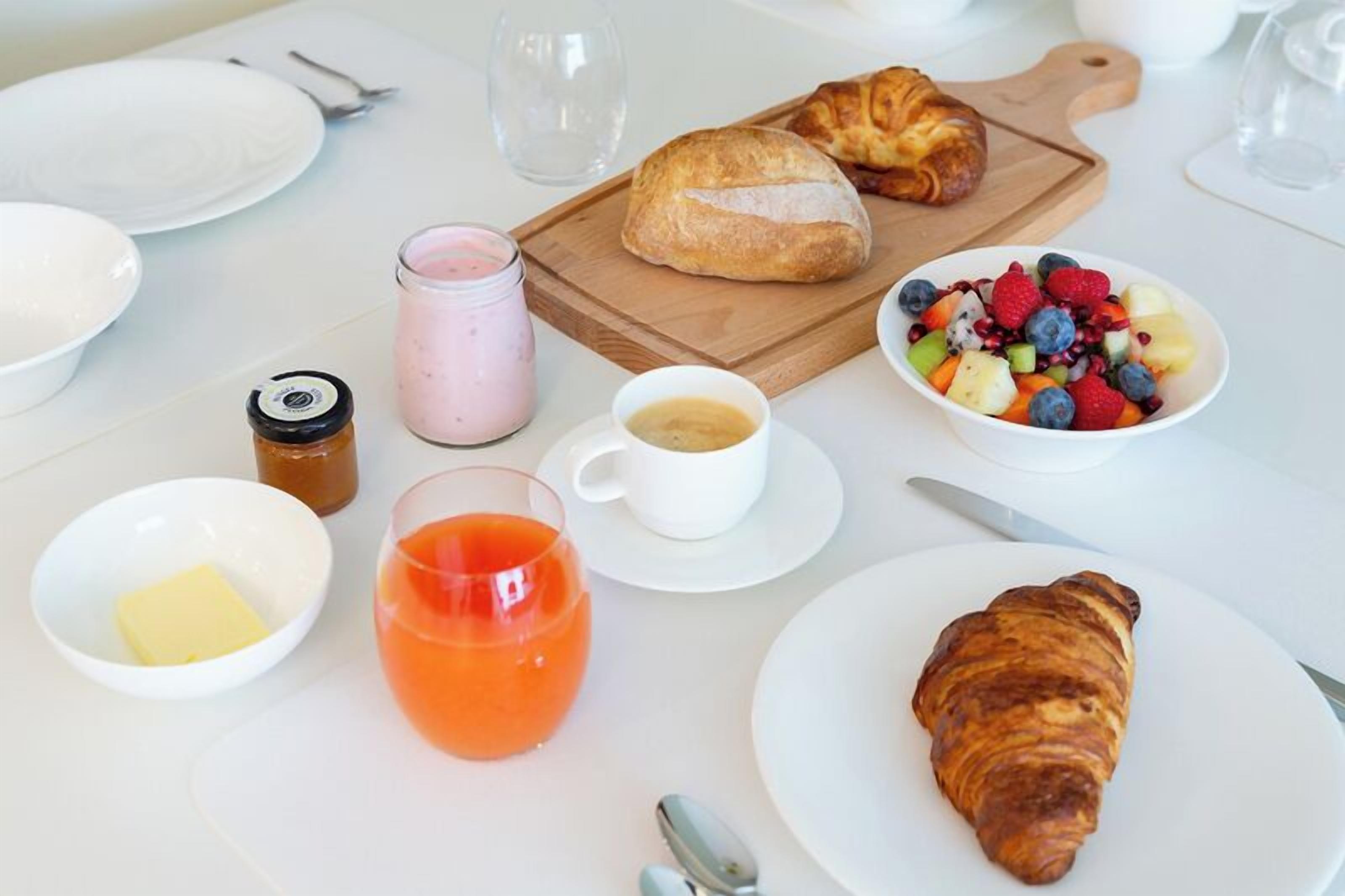 En frukostuppläggning med croissanter, fruktsallad, kaffe och juice.