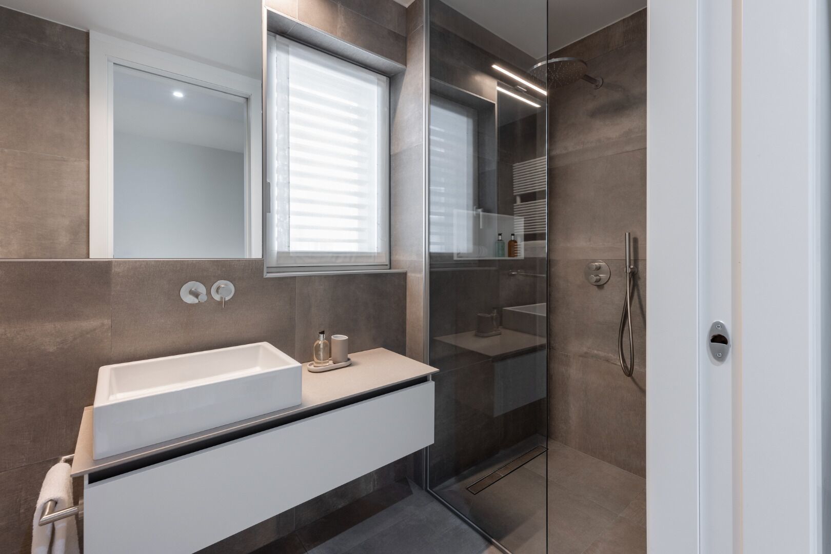 A modern bathroom with a large mirror, a white sink, and a glass-enclosed shower area.
