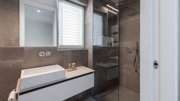 A modern bathroom with a large mirror, a white sink, and a glass-enclosed shower area.