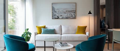 A modern living room with a white sofa, teal chairs, a small round table, and a cityscape painting on the wall.