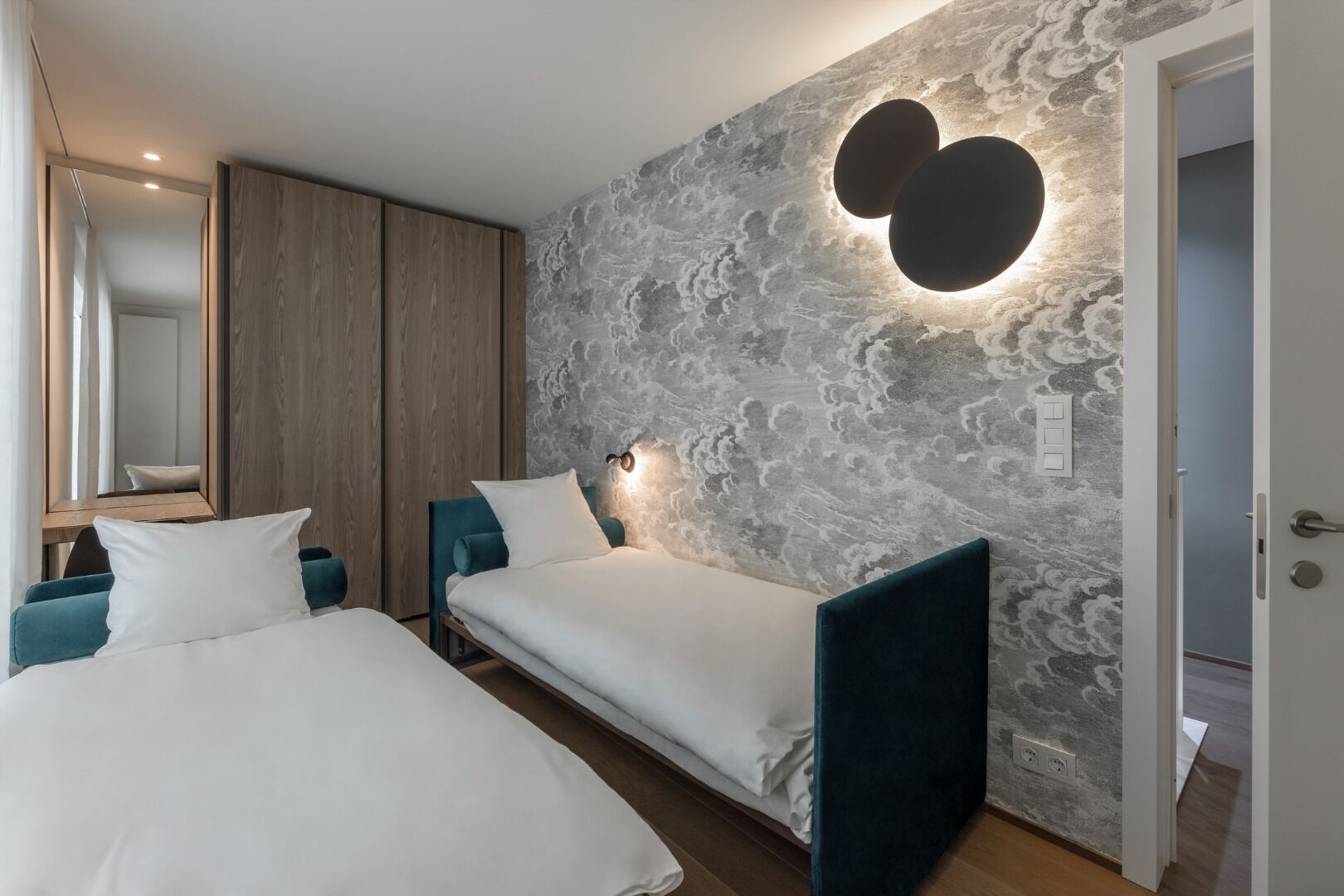 Een moderne slaapkamer met twee bedden, een grote spiegel en een gestructureerde wand met een hartvormige lamp.