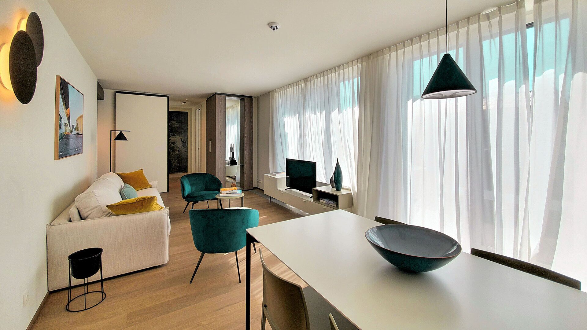 A modern living room with a sofa, chairs, a dining table, and a TV.