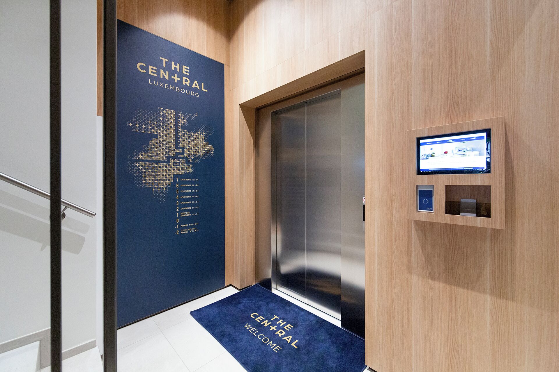 Un ascenseur moderne, avec un intérieur contemporain, un écran numérique et un paillasson d’accueil.