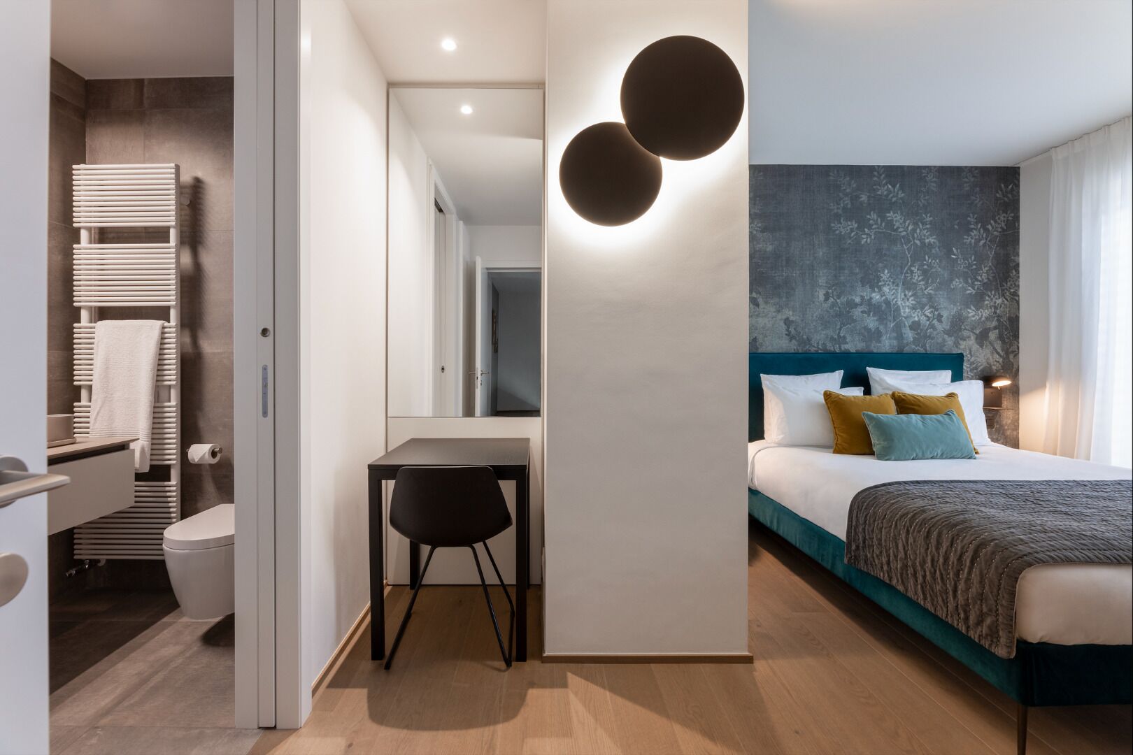 Una habitación de hotel moderna con baño privado, un escritorio y una cama con cabecero azul.