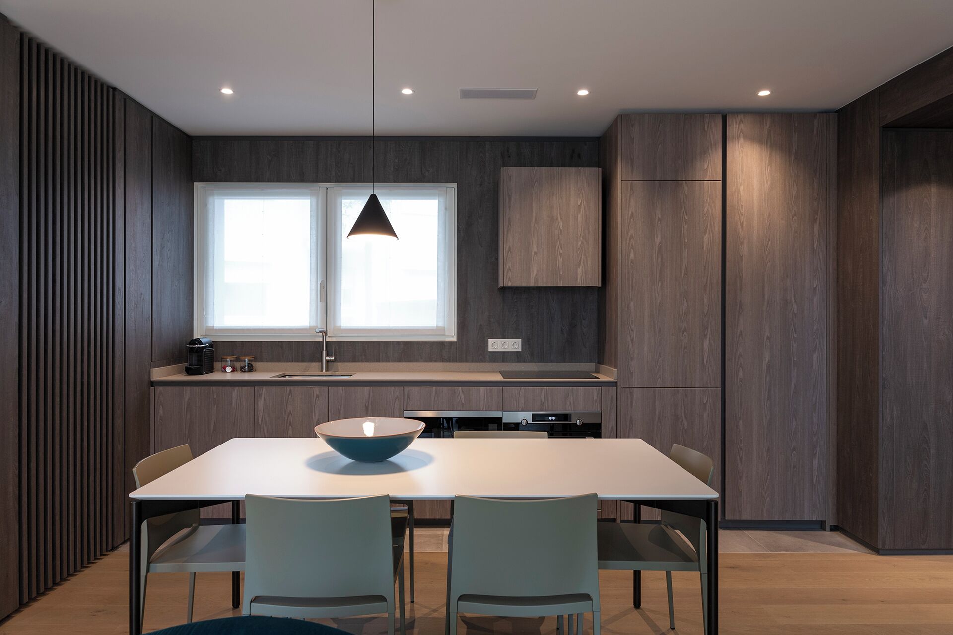 A modern kitchen with a white countertop, a large window, and a dining area with a table and chairs.
