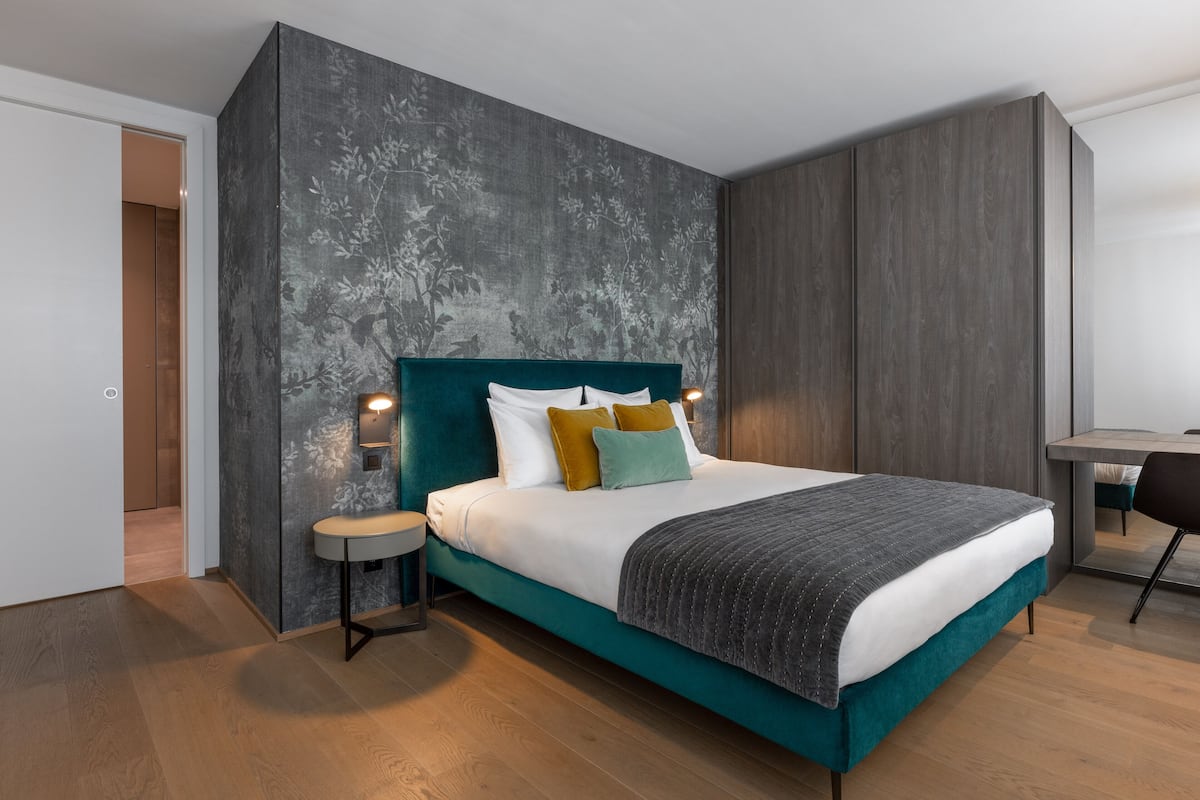Une chambre moderne avec un lit de couleur turquoise, une petite table de chevet et une commode.