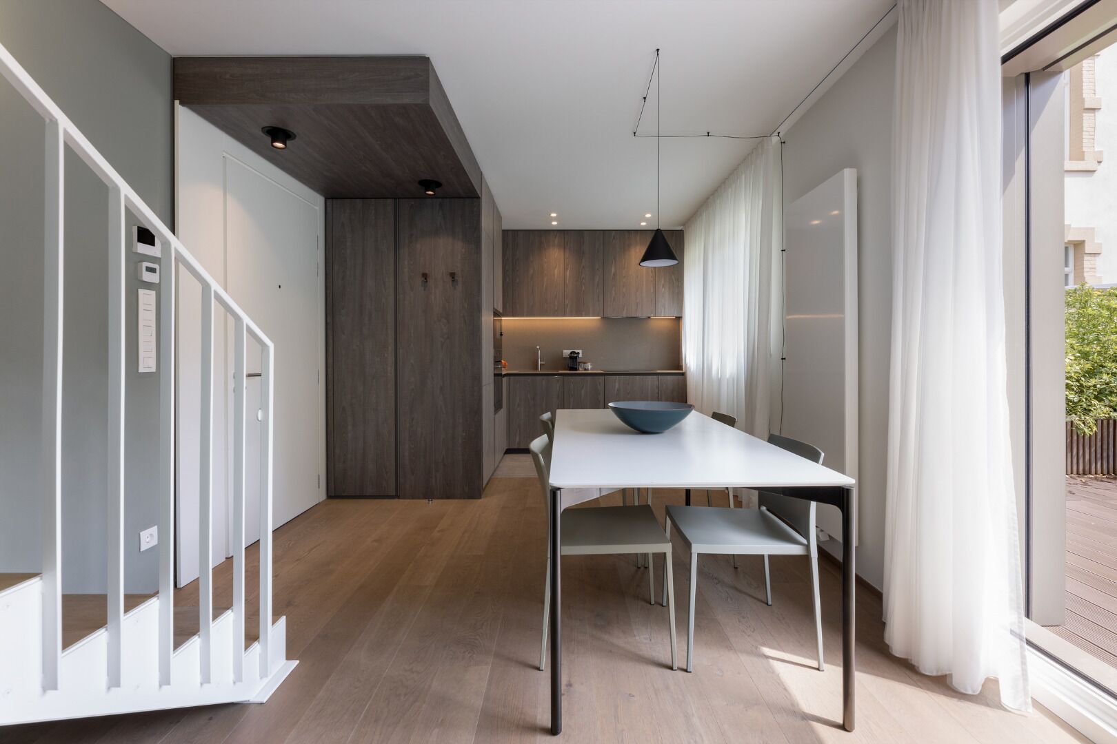 Une cuisine moderne avec des meubles en bois, une table à manger avec des chaises et une grande fenêtre avec des rideaux.
