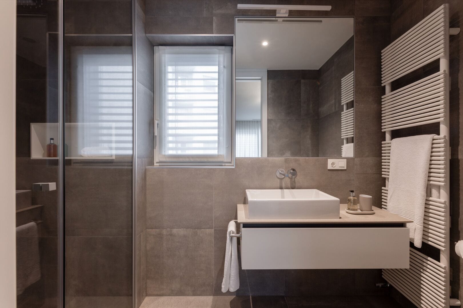 A modern bathroom with a glass shower enclosure, a white sink, and a towel rack.