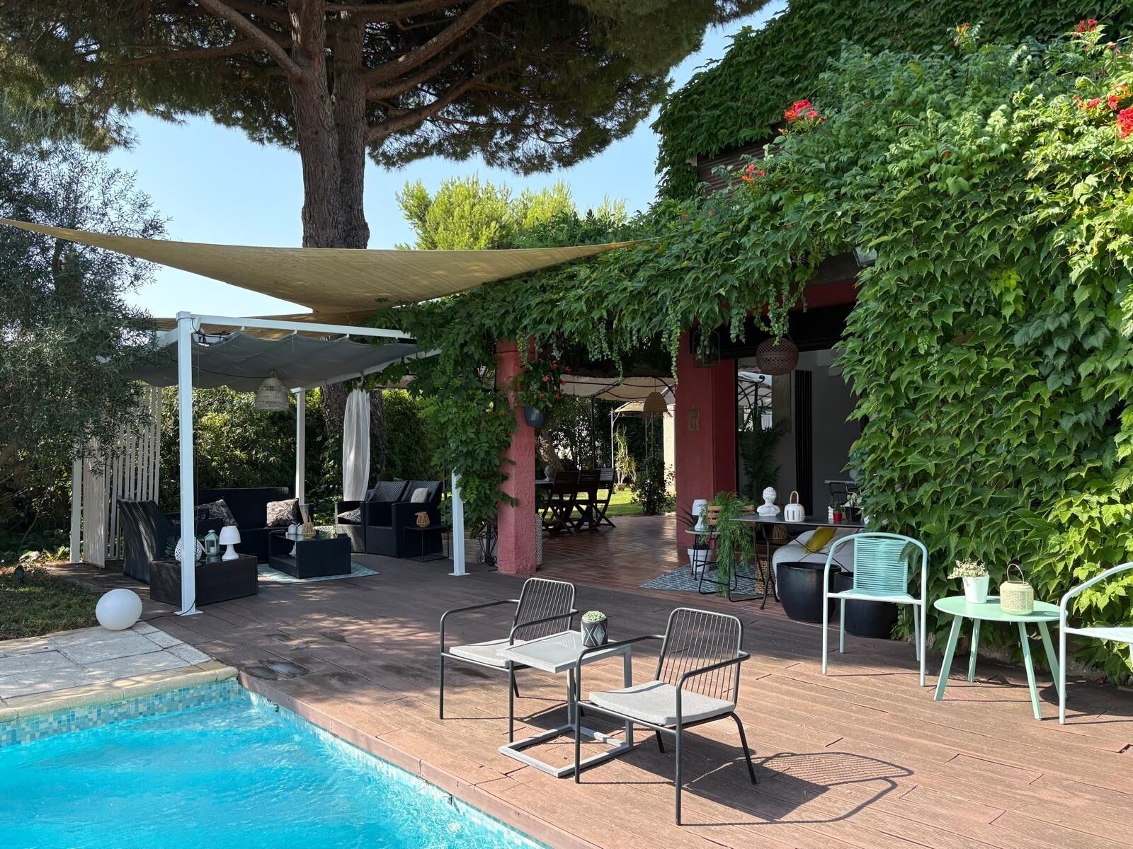 An outdoor pool area with a covered seating area, lounge chairs, and a pergola providing shade.