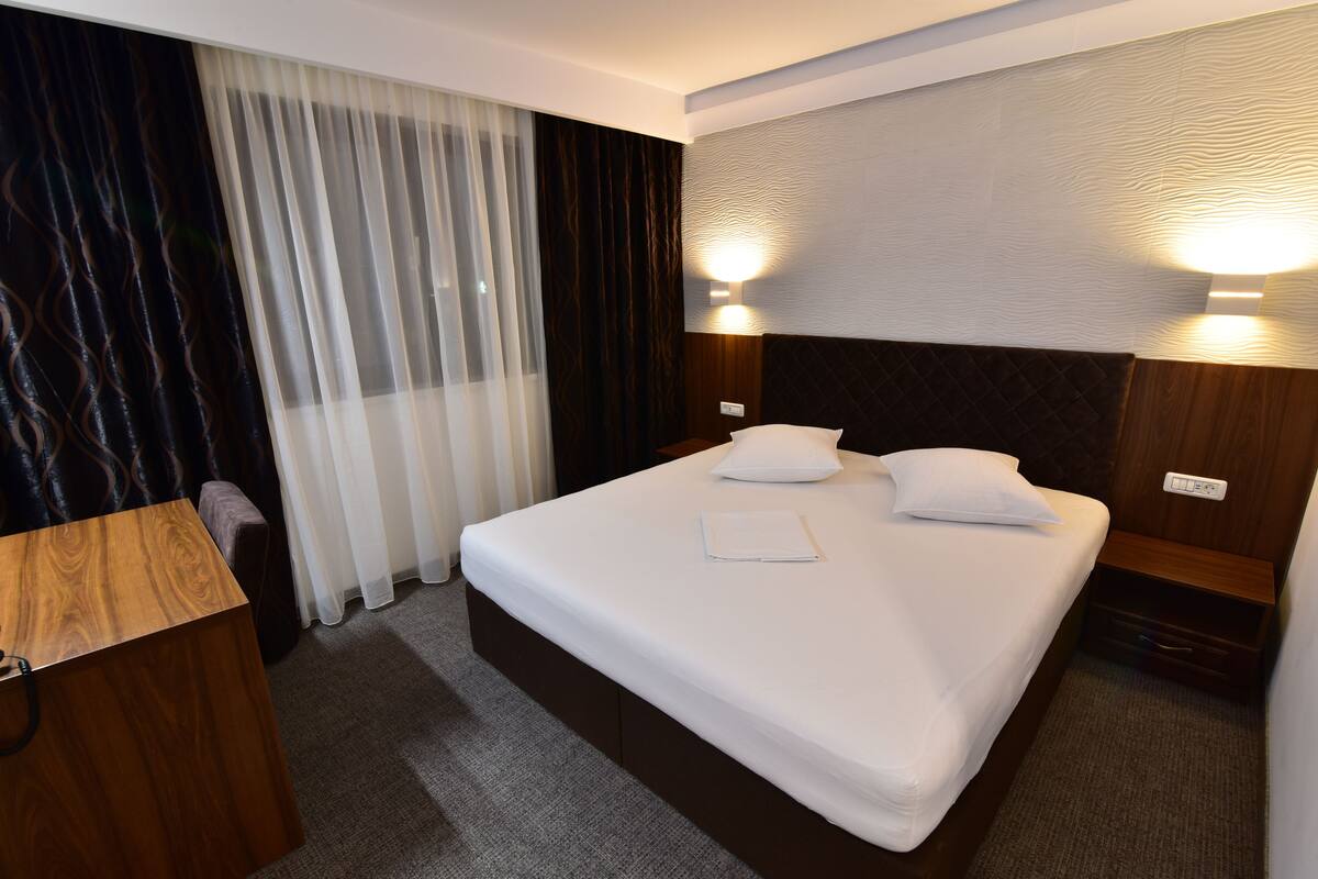 A neatly made bed with white linens, a wooden headboard, and two bedside lamps.