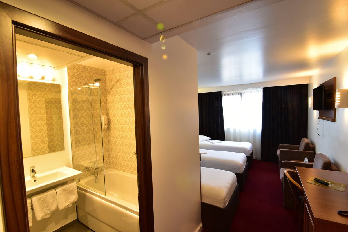 A hotel room with a bathroom, a shower, a bed, a desk, and a TV.