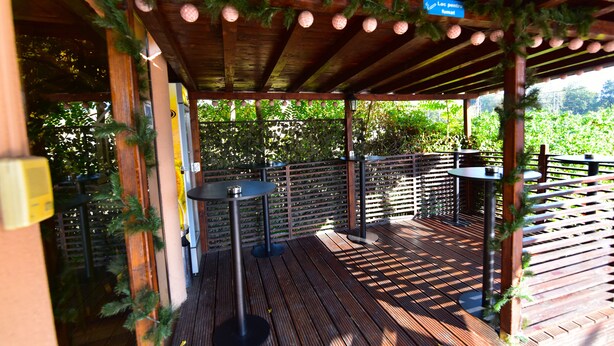 An outdoor wooden deck with tables and chairs, surrounded by greenery and a wooden fence. - Hotel Forum (Ploiesti)