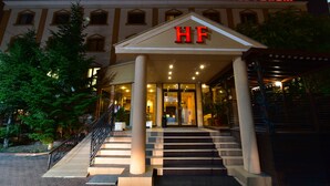 A hotel entrance with a prominent 'HF' sign, a staircase leading up to the entrance, and a well-lit facade. - Hotel Forum (Ploiesti)