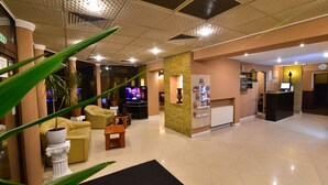 Un vestíbulo de hotel con mostrador de recepción, zona de estar y televisor.