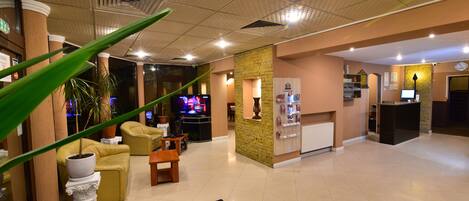 Eine Hotelhalle mit Empfangstresen, Sitzgelegenheiten und einem Fernseher.