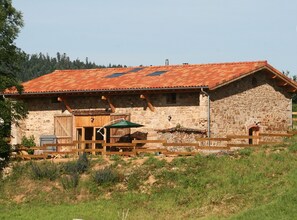 A rustic stone building with a red-tiled roof, wooden fence, and a small patio area. - Eco-cottage with countryside view - 11 guests (Saint-Romain-d'Urfé)