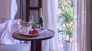 Un balcon avec une table dressée pour deux personnes, agrémentée d’une bouteille de champagne, d’une assiette de fraises et d’un vase rempli de fleurs.
