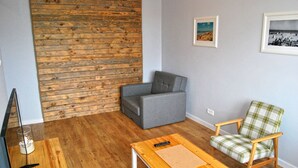 A living room with a wooden wall panel, a grey sofa, a wooden coffee table, and a plaid armchair. - HelApartamenty - Apartament Bałtyk (Hel)