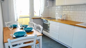 A kitchen with white cabinets, a wooden countertop, and a dining table set with blue plates and wine glasses. - HelApartamenty - Apartament Bałtyk (Hel)