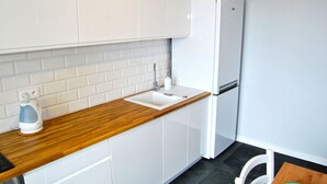 A modern kitchen with white cabinets, a wooden countertop, a white sink, and a white refrigerator. - HelApartamenty - Apartament Bałtyk (Hel)