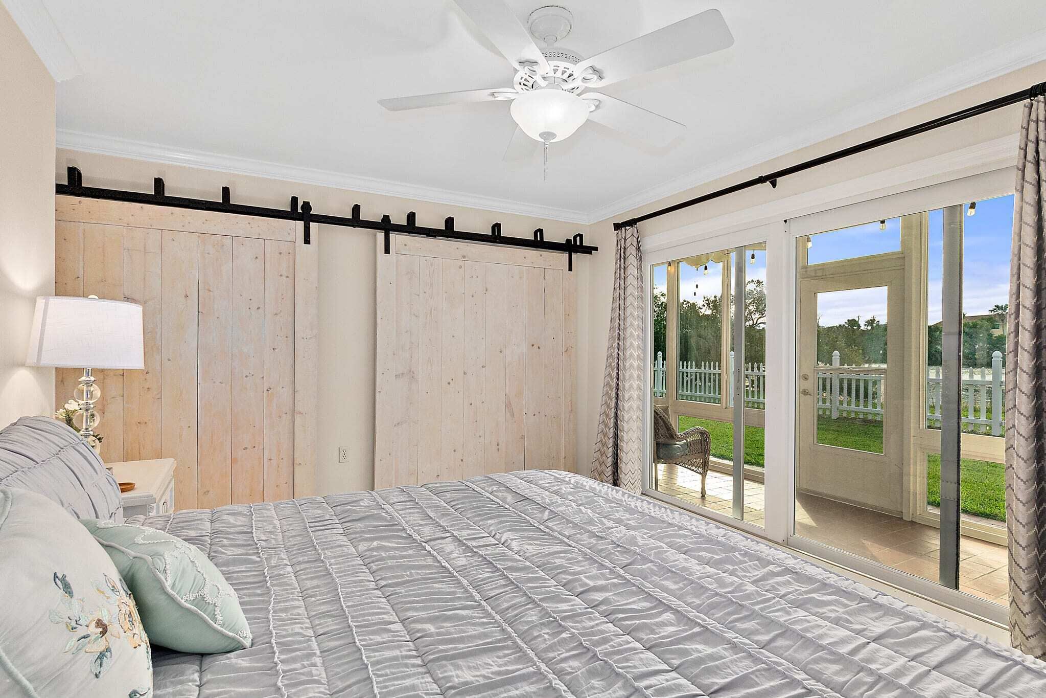 Ein Schlafzimmer mit einem großen Bett, einem Deckenventilator, einem Holzschrank und einer Glastür zum Balkon.