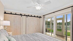 A bedroom with a large bed, a ceiling fan, a wooden wardrobe, and a sliding glass door leading to a balcony. - Island Oasis l Steps to the Ocean l 2 Pools (St. Augustine)