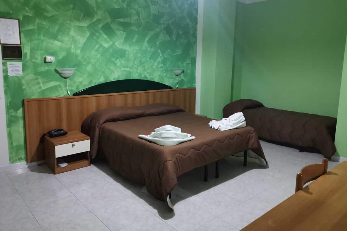 Hotellihuone, jossa on sänky, yöpöytä, lamppu ja pieni työpöytä.