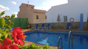 A swimming pool with blue tiles, surrounded by lounge chairs and a lifebuoy on a white wall. - Hostal Manolo (Garrucha)