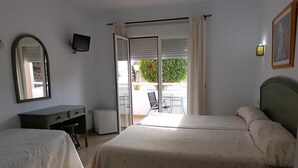 A bedroom with two beds, a desk, a chair, a television, and a sliding glass door leading to an outdoor area. - Hostal Manolo (Garrucha)