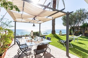 An outdoor patio with a table and chairs, a pergola, and a view of the sea.