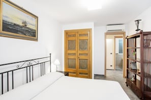 Une chambre à coucher comprenant un lit, une armoire en bois, une bibliothèque, un tableau et une porte donnant sur une autre pièce.