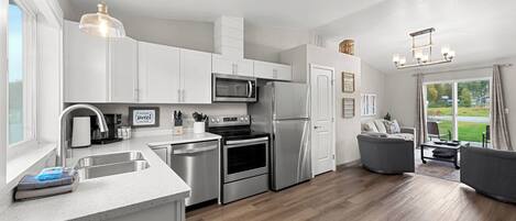 A modern kitchen with stainless steel appliances, a large island with a sink, and a dining area with a grey sofa and table.