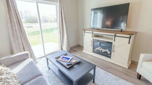 Un soggiorno moderno con una TV a schermo piatto montata su un mobile in legno, un divano, un tavolino da caffè e una porta scorrevole in vetro che dà su un giardino.