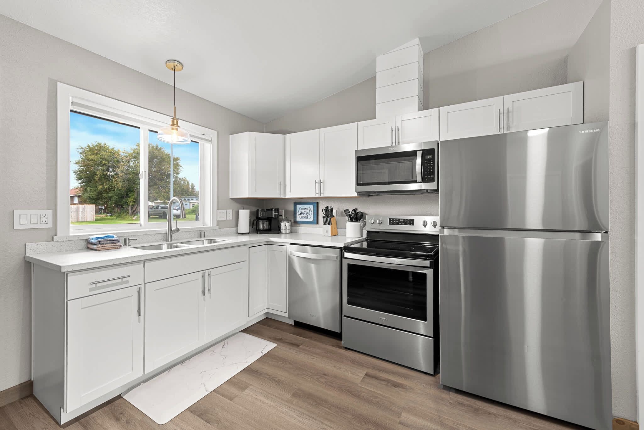 A modern kitchen with white cabinetry, stainless steel appliances, and a large window offering a view of the outdoors.