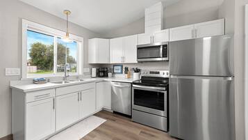 A modern kitchen with white cabinetry, stainless steel appliances, and a large window offering a view of the outdoors.